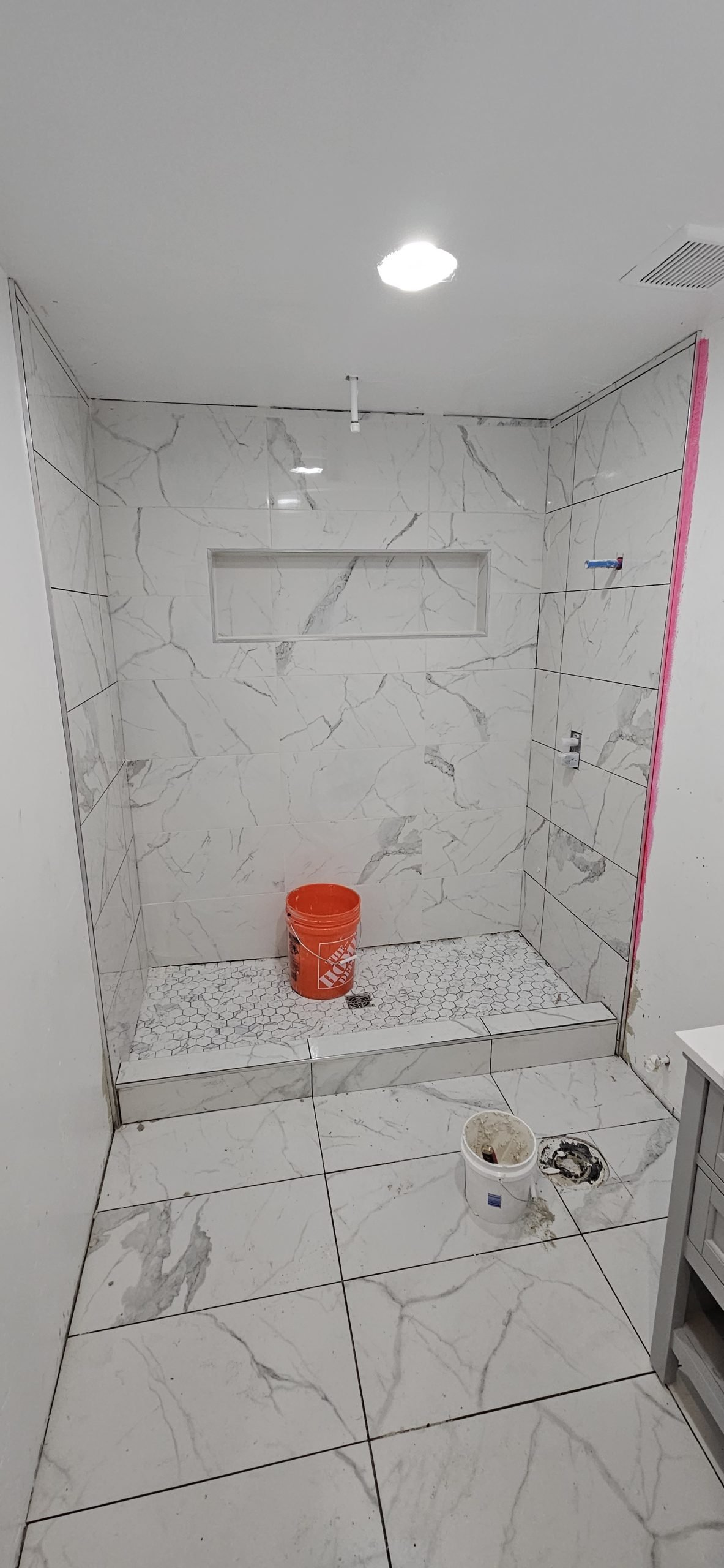 Bathroom remodel in progress featuring a marble tile shower with a built-in shelf.