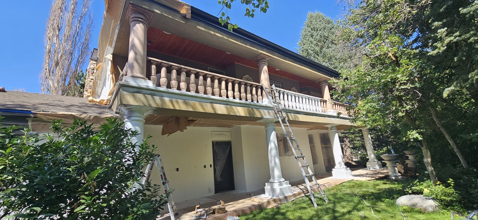 Utah home undergoing exterior painting with ladders, showcasing detailed architectural elements.