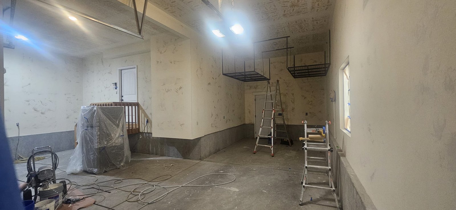 Garage interior being prepared for painting, showing exposed walls, ladders, and painting equipment, in Utah